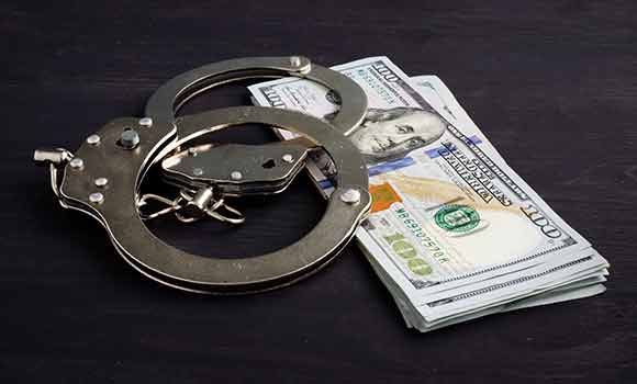 Handcuffs beside a stack of U.S. dollar bills on a dark surface