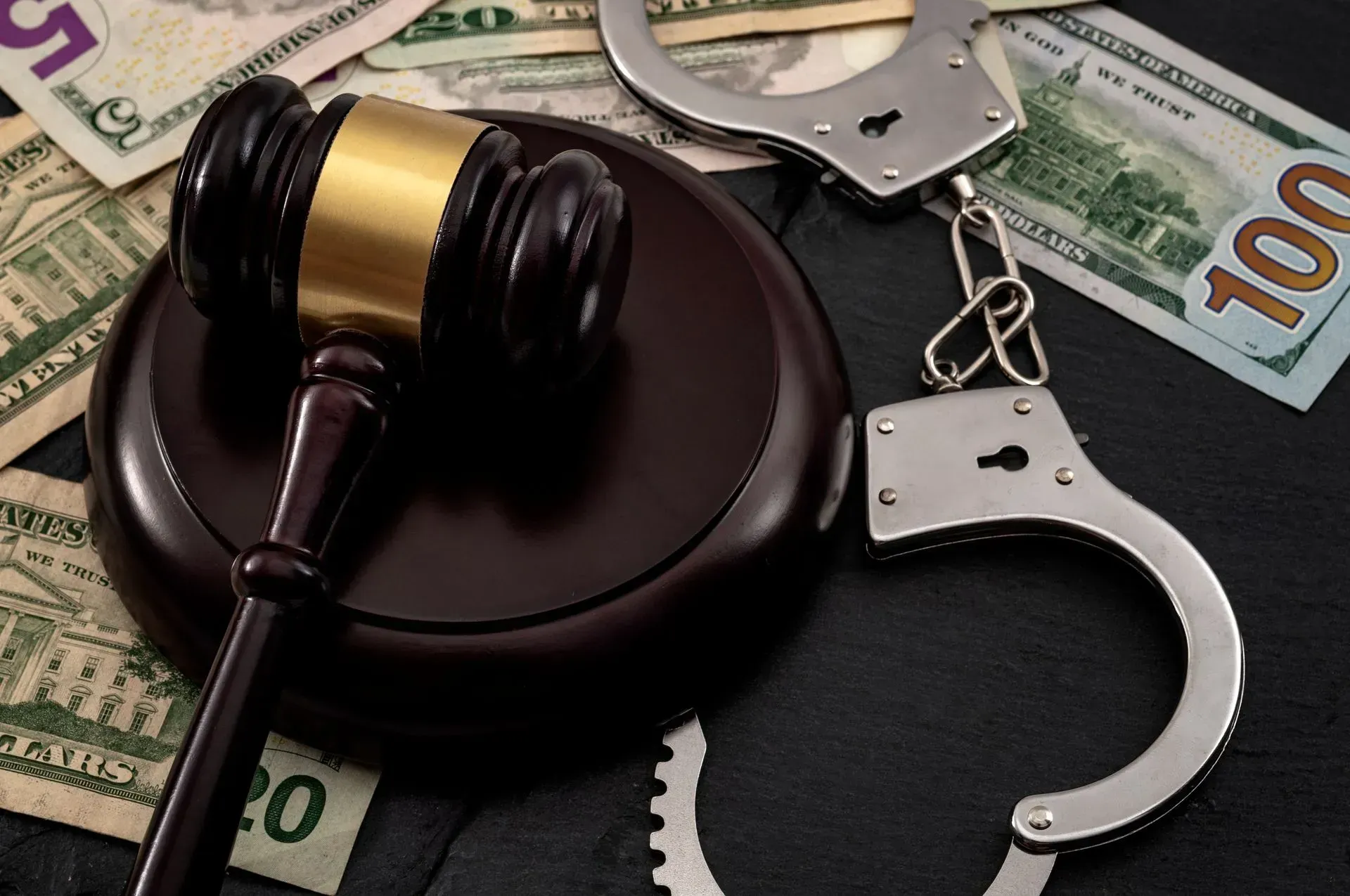 Handcuffs beside a judge’s gavel on a stack of currency, symbolizing crime and justice