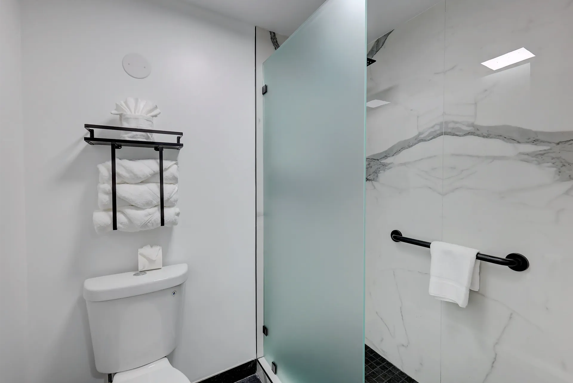 Bathroom with white walls, toilet, shower with frosted glass door, and black accents.