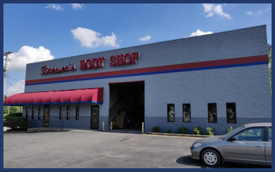 Gray, industrial-style building named Brewer's Body Shop with a red awning and a gray car parked in the front lot.