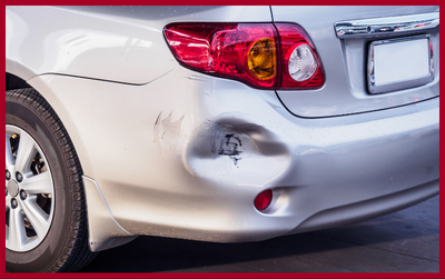 A silver car showing a dented rear bumper with paint damage near the taillight.