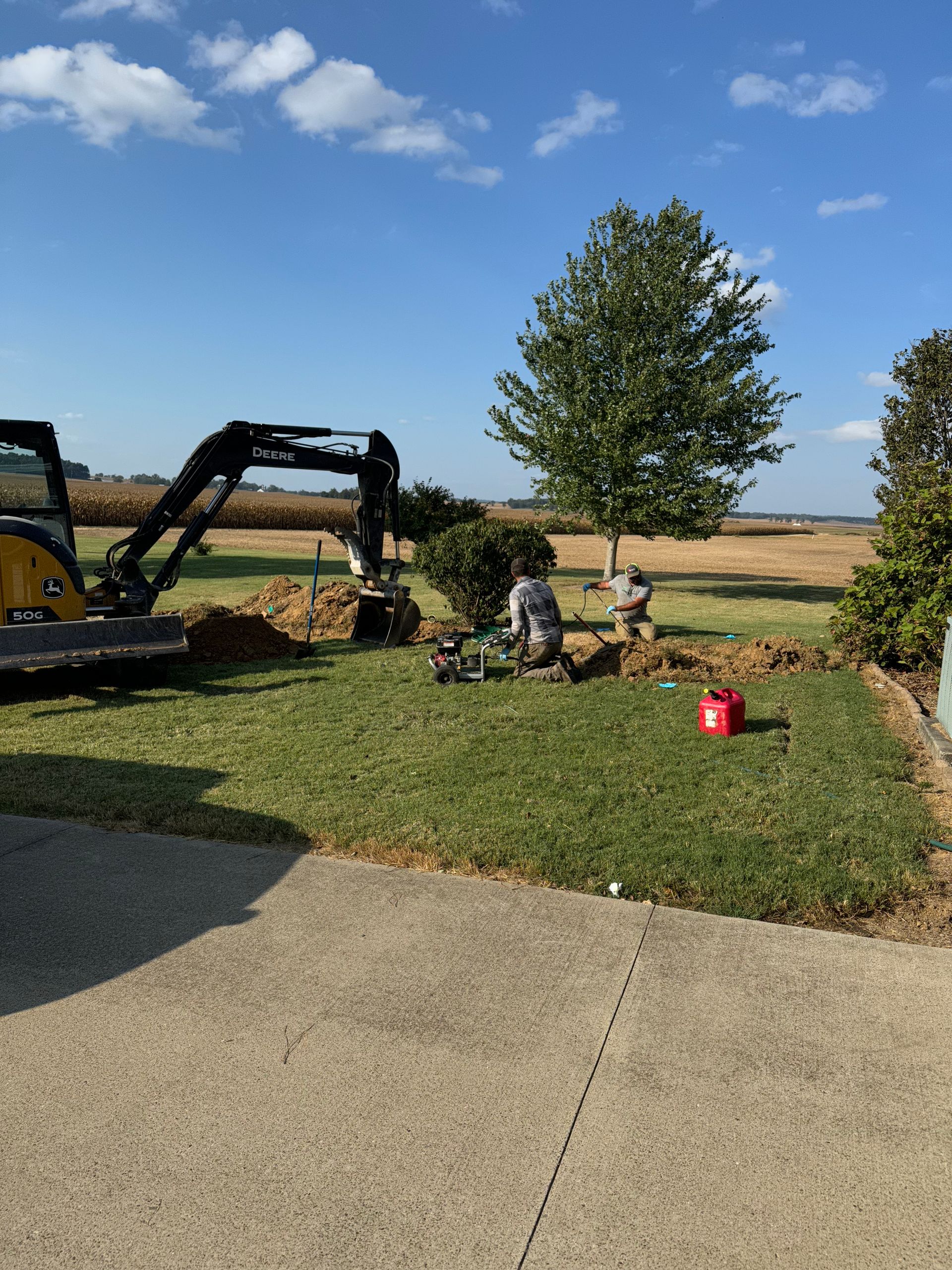 A yellow excavator is digging a hole in a yard.