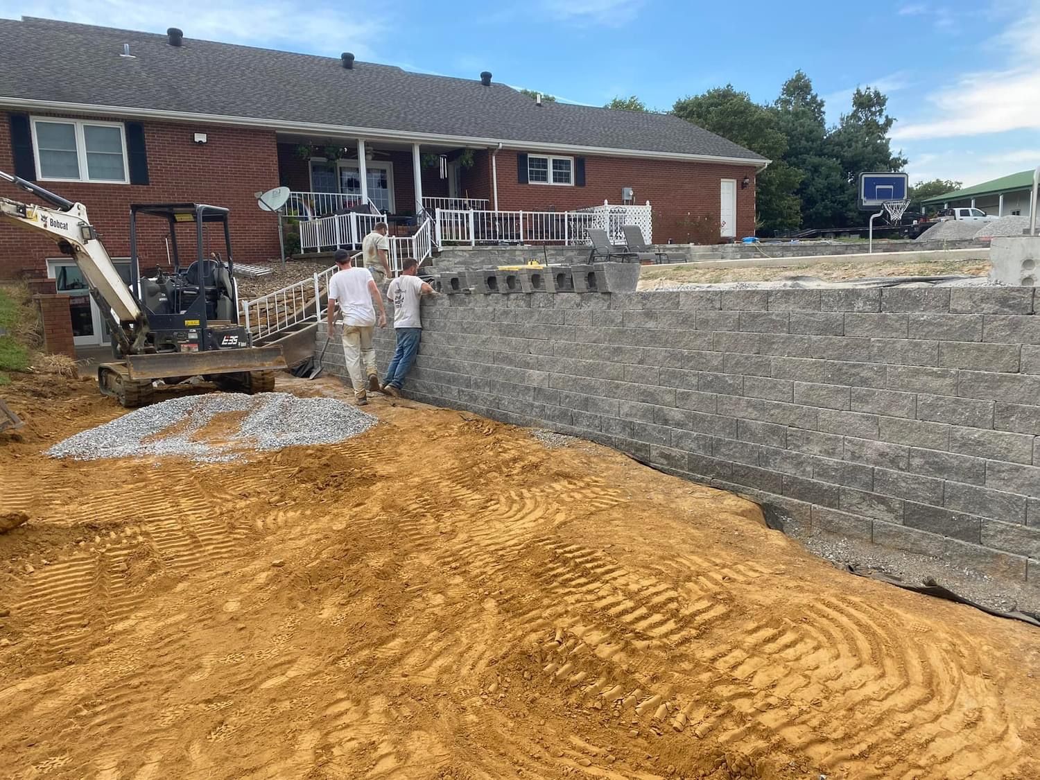 A couple of men standing next to a pile of dirt in front of a house.