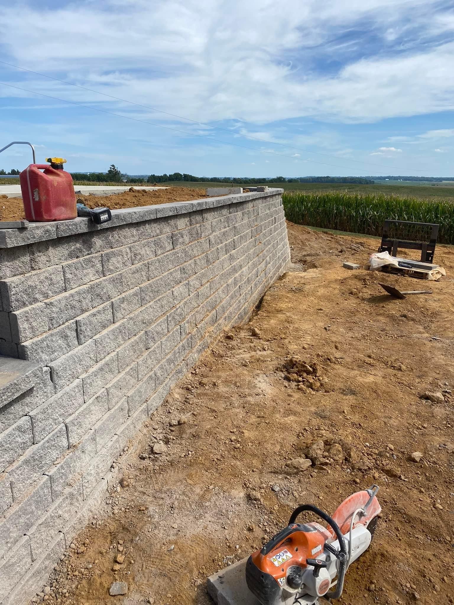 A stihl chainsaw is sitting in the dirt next to a brick wall.
