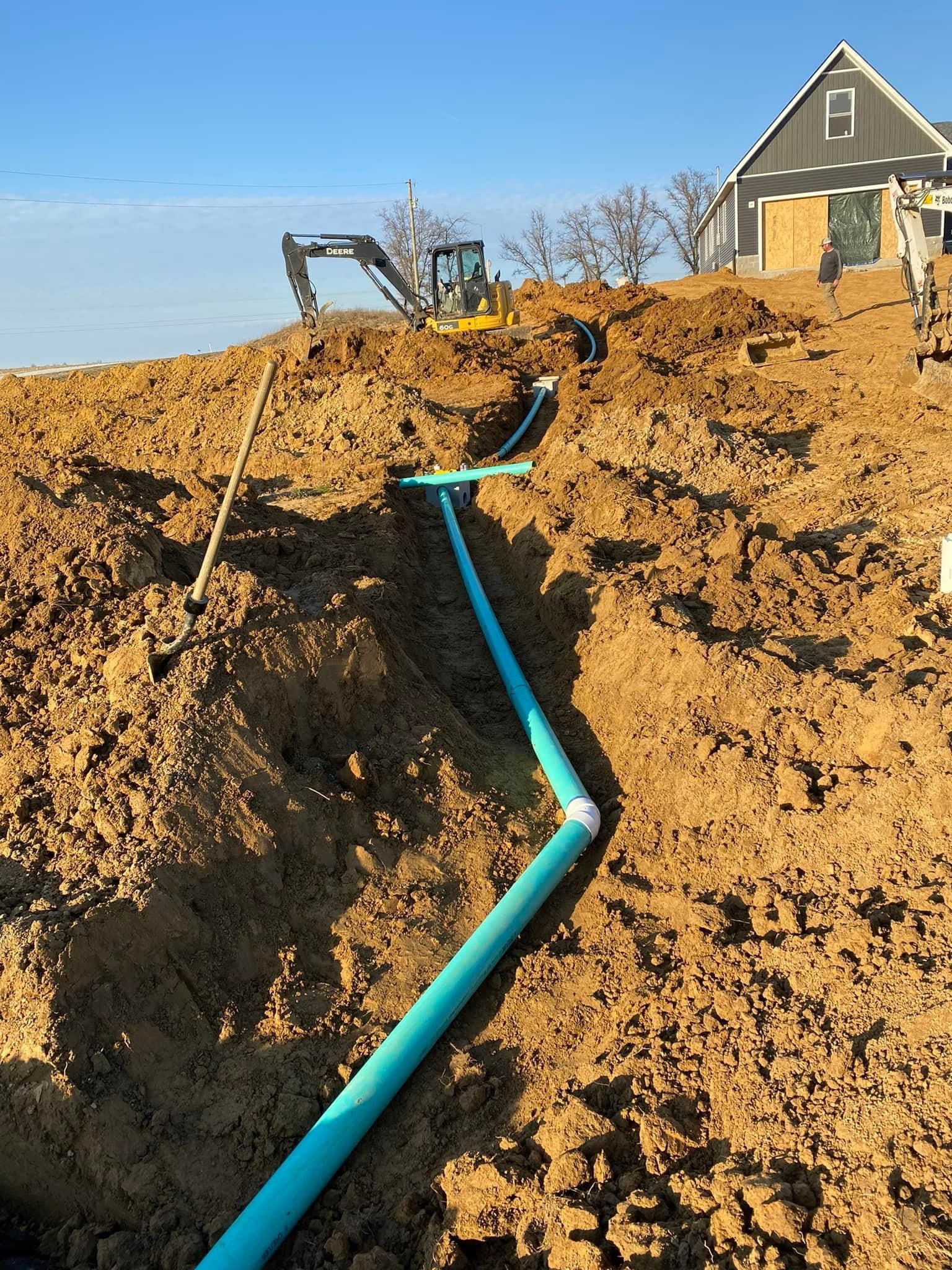 A green pipe is being installed in the dirt in front of a house.