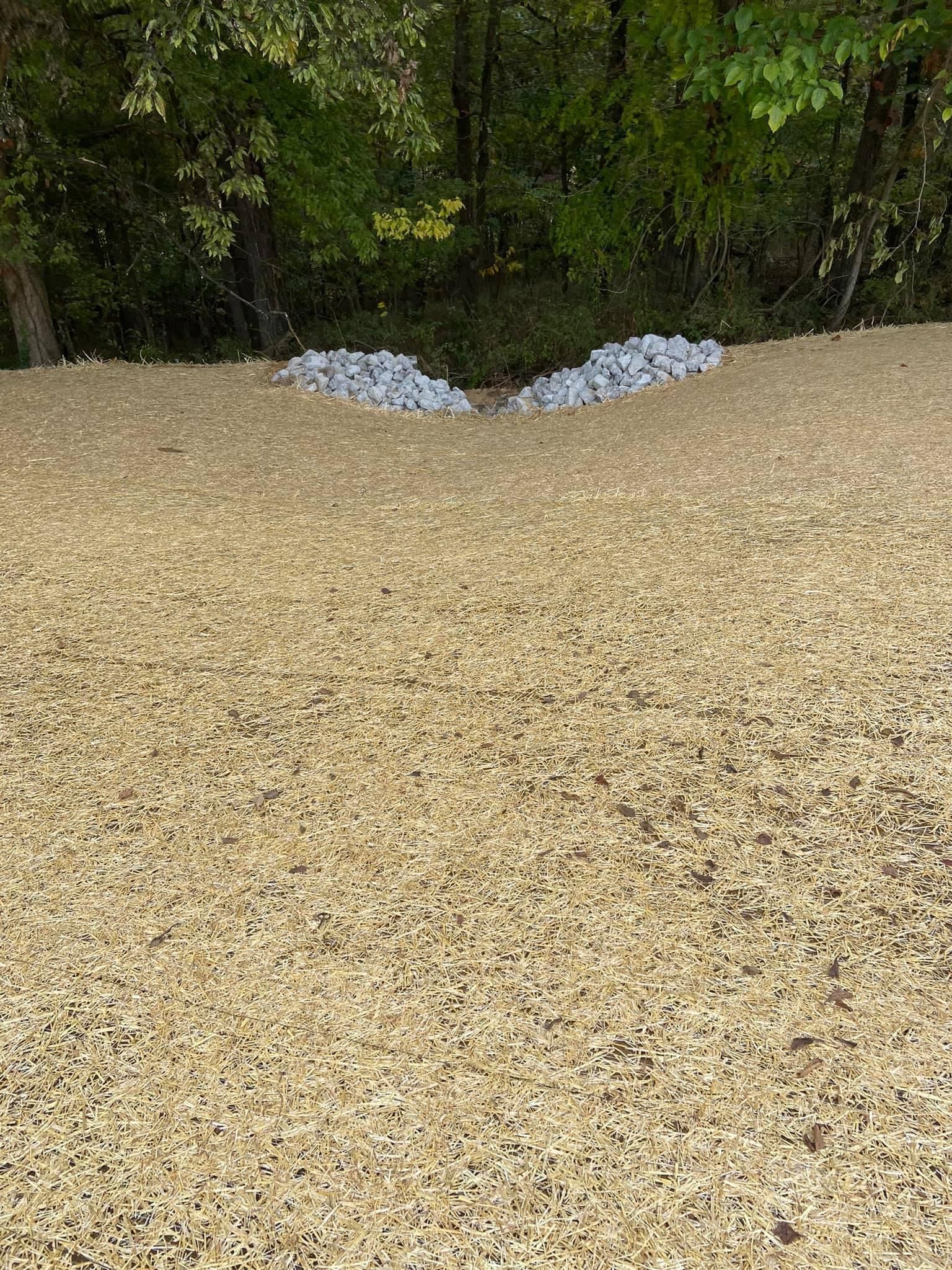 A pile of gravel and rocks in a field with trees in the background.