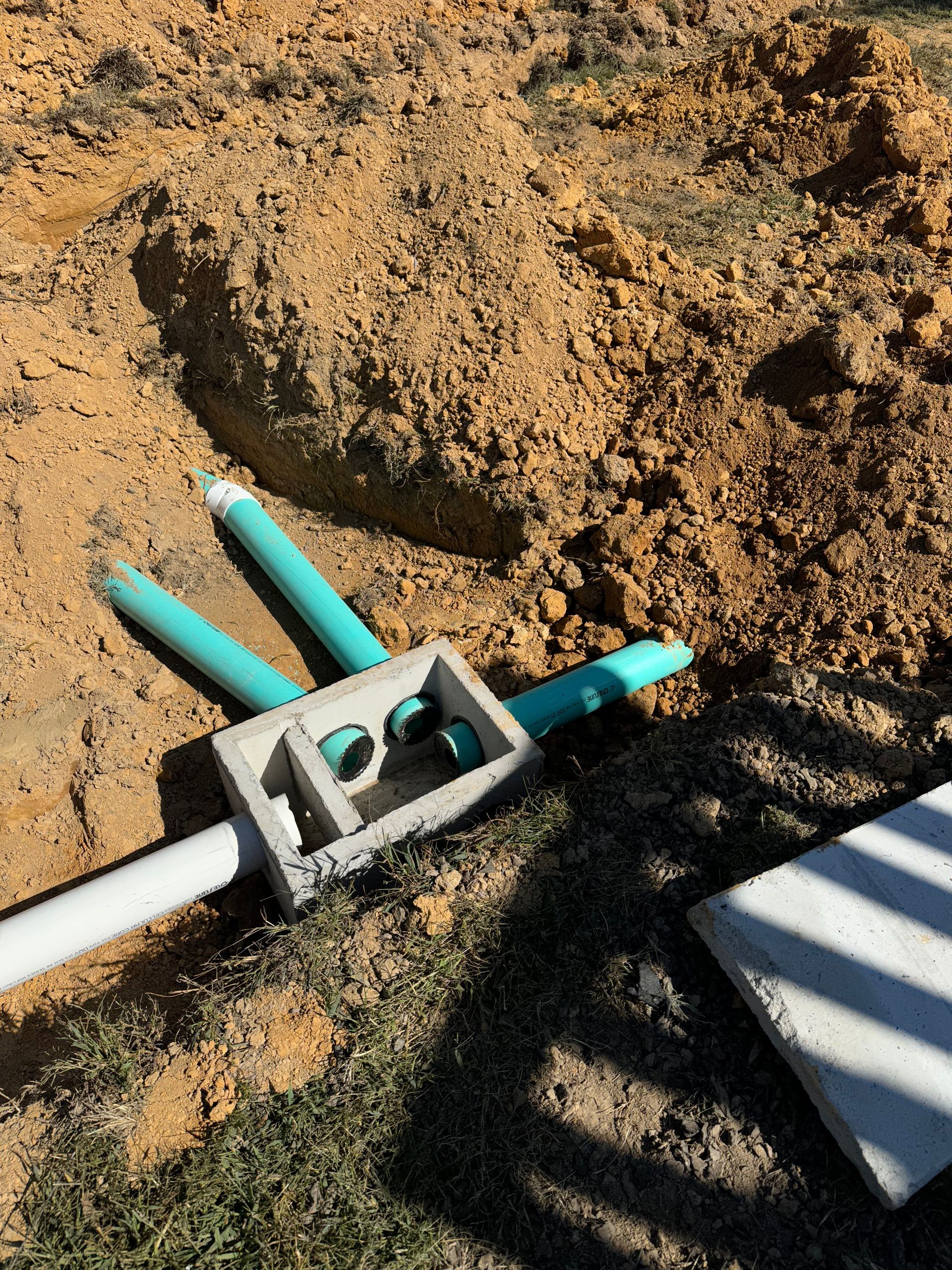 A pipe is laying in the dirt next to a concrete slab.