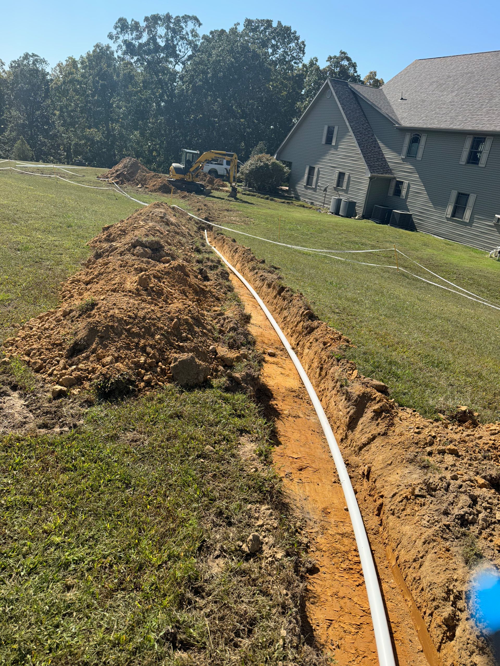 A white pipe is laying in the dirt in front of a house.