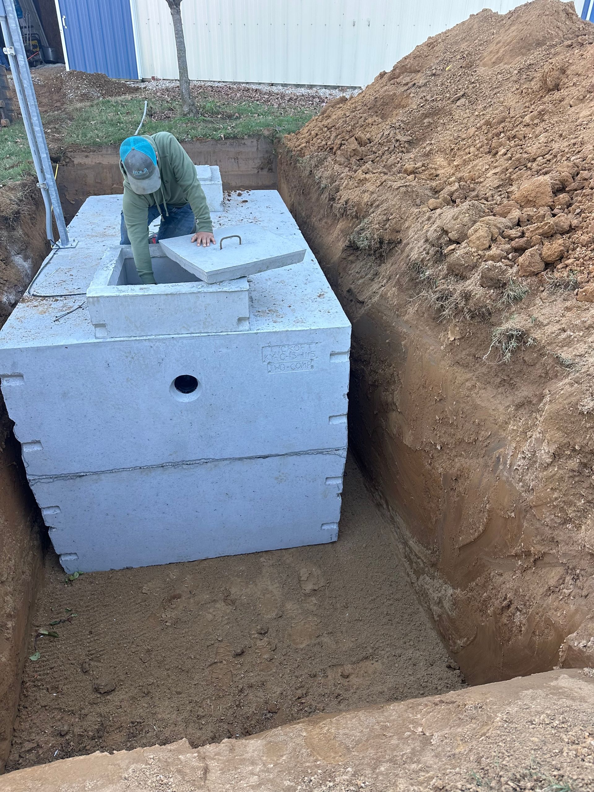 A man is standing in a hole next to a septic tank.