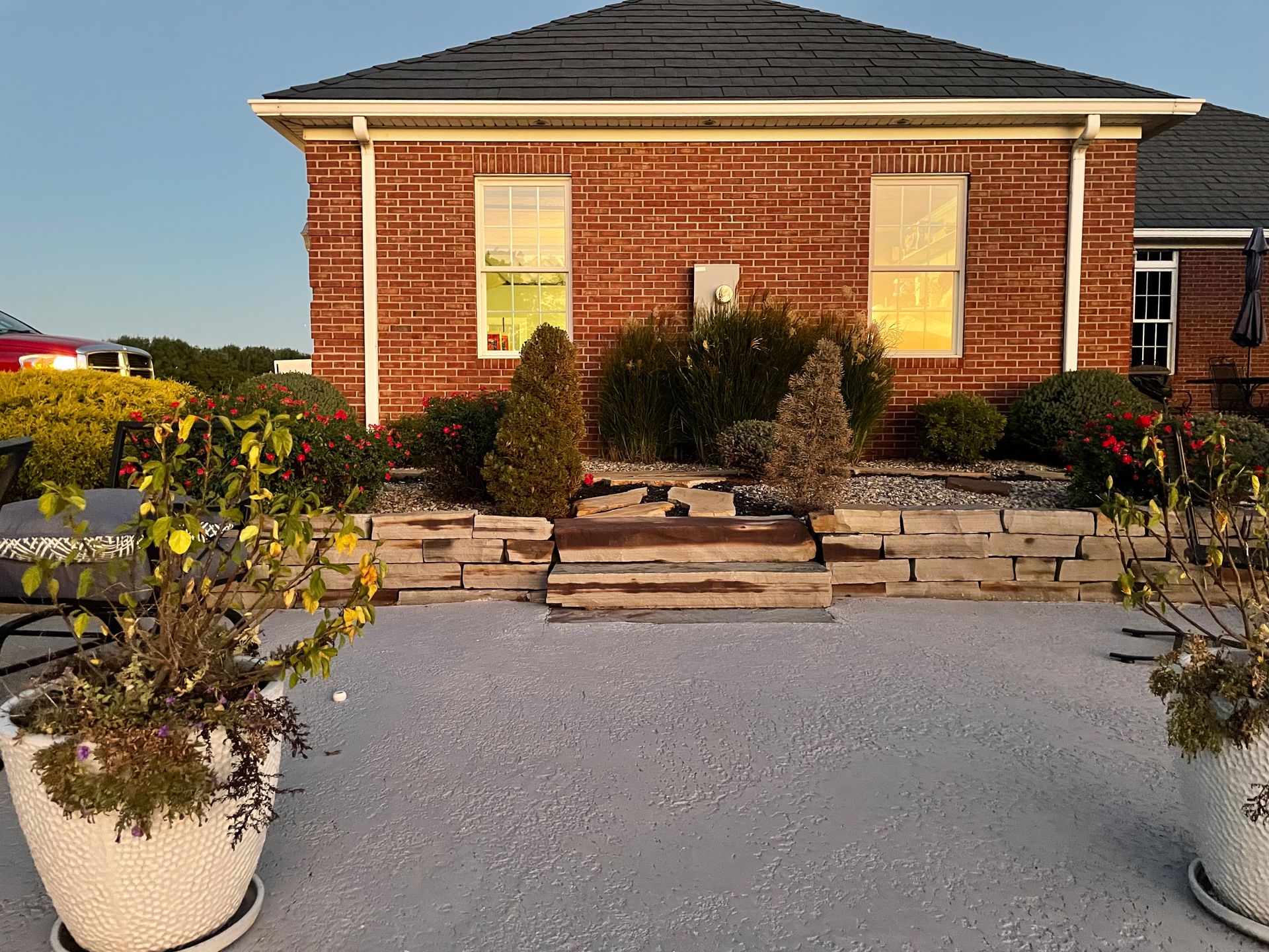 A brick house with a black roof is surrounded by potted plants