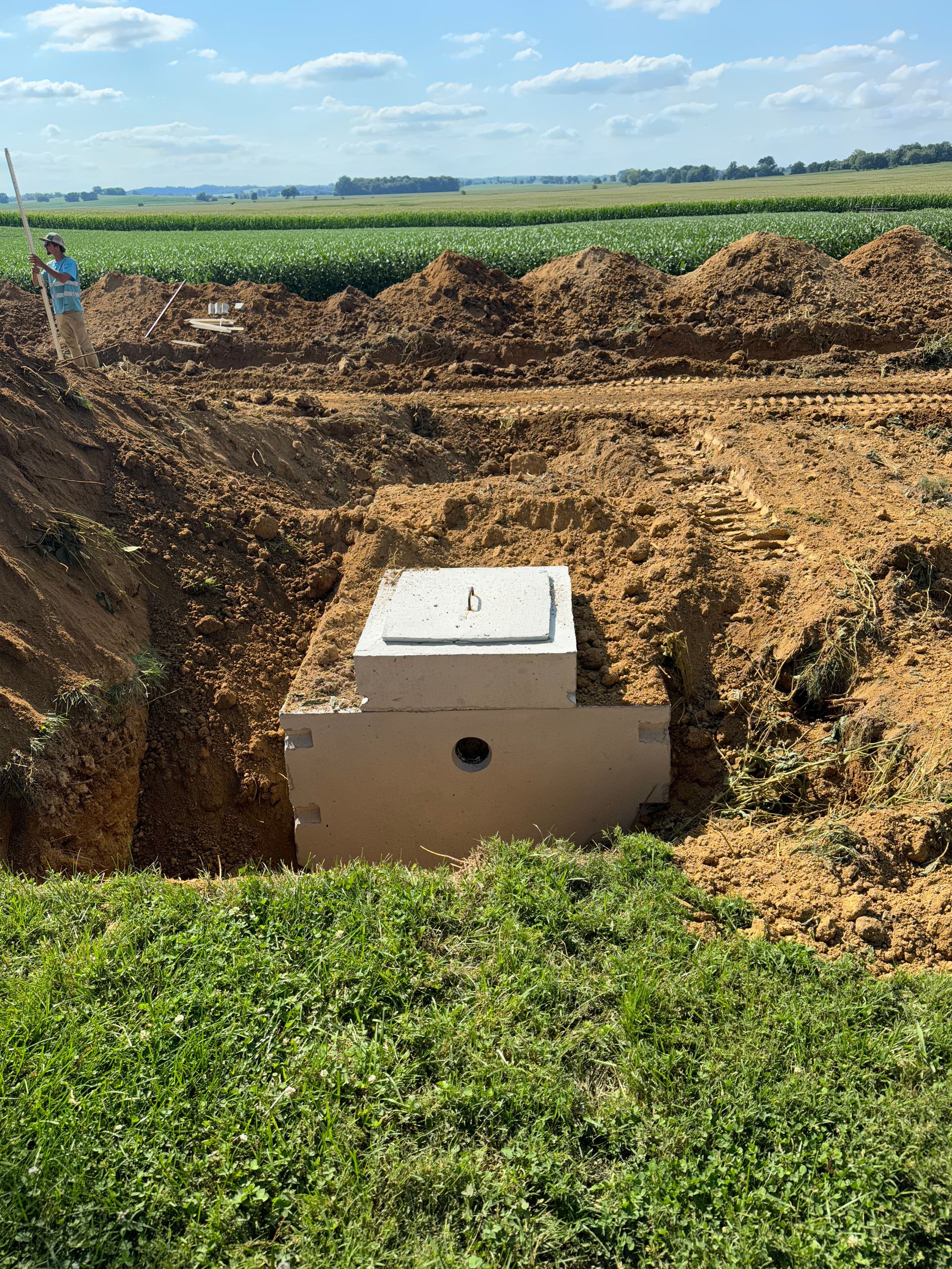 A man is standing in the dirt next to a concrete box in the middle of a field.