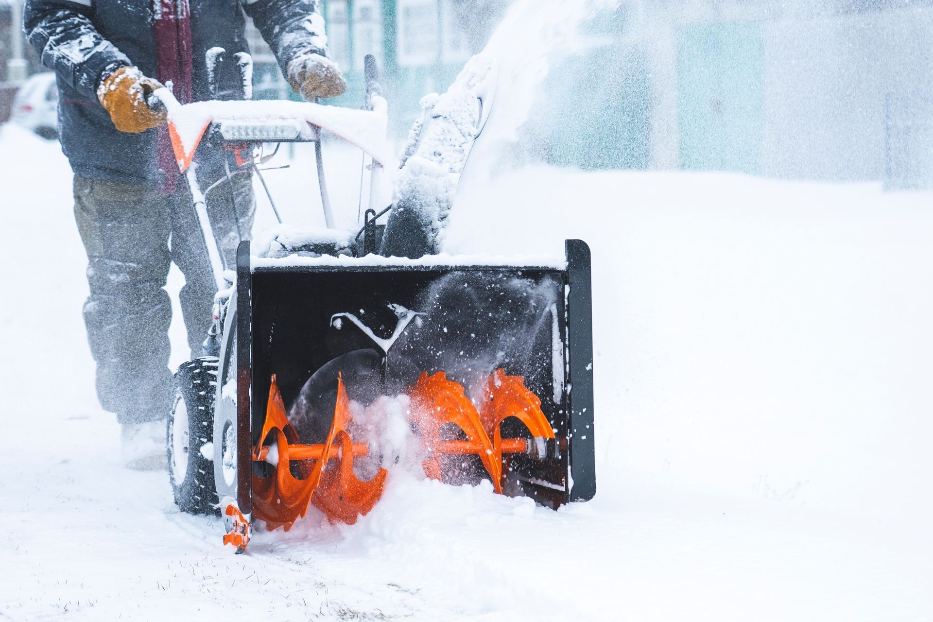 A man is using a snow blower to remove snow from a sidewalk.