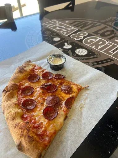 Slice of pepperoni pizza on parchment paper with a small dipping cup on a black table.