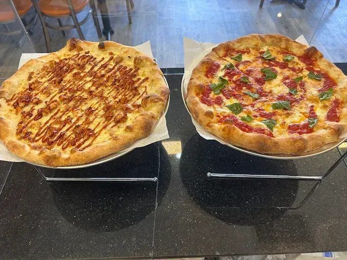 Two pizzas on display stands: one plain, one topped with colorful ingredients.