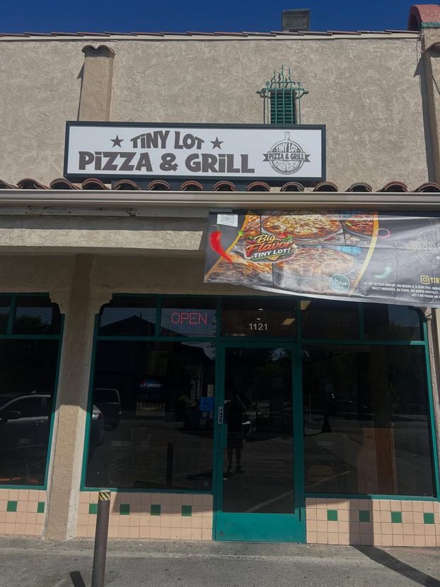Tiny Lot Pizza & Grill storefront with teal doors and a banner over the entrance