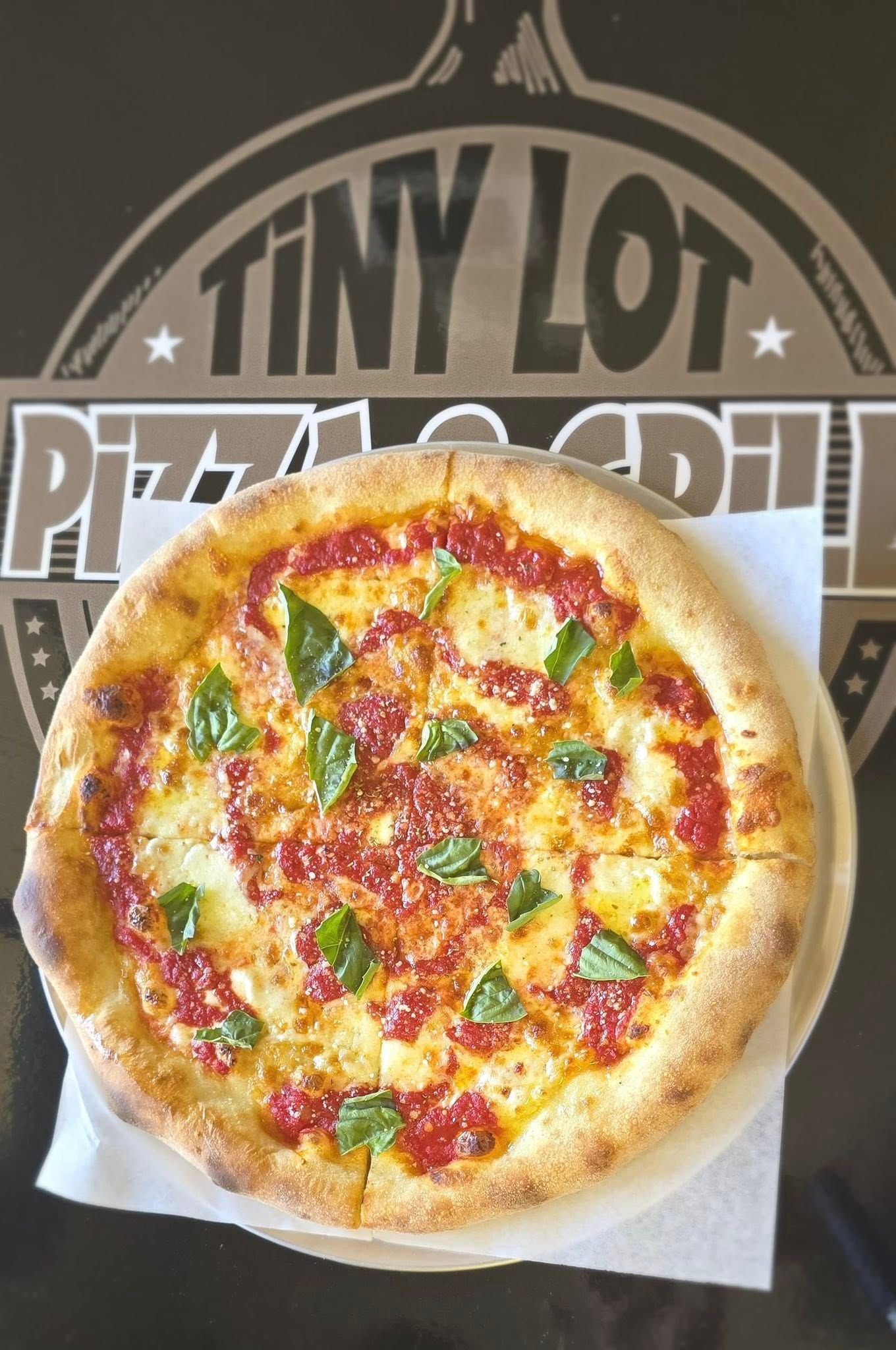 Pizza on a white tray in front of a Tiny Lot Pizza sign