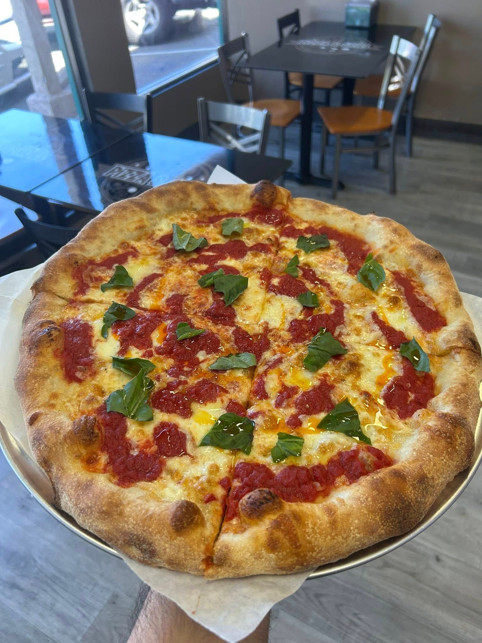 Cheese pizza topped with basil on a metal stand in a casual restaurant
