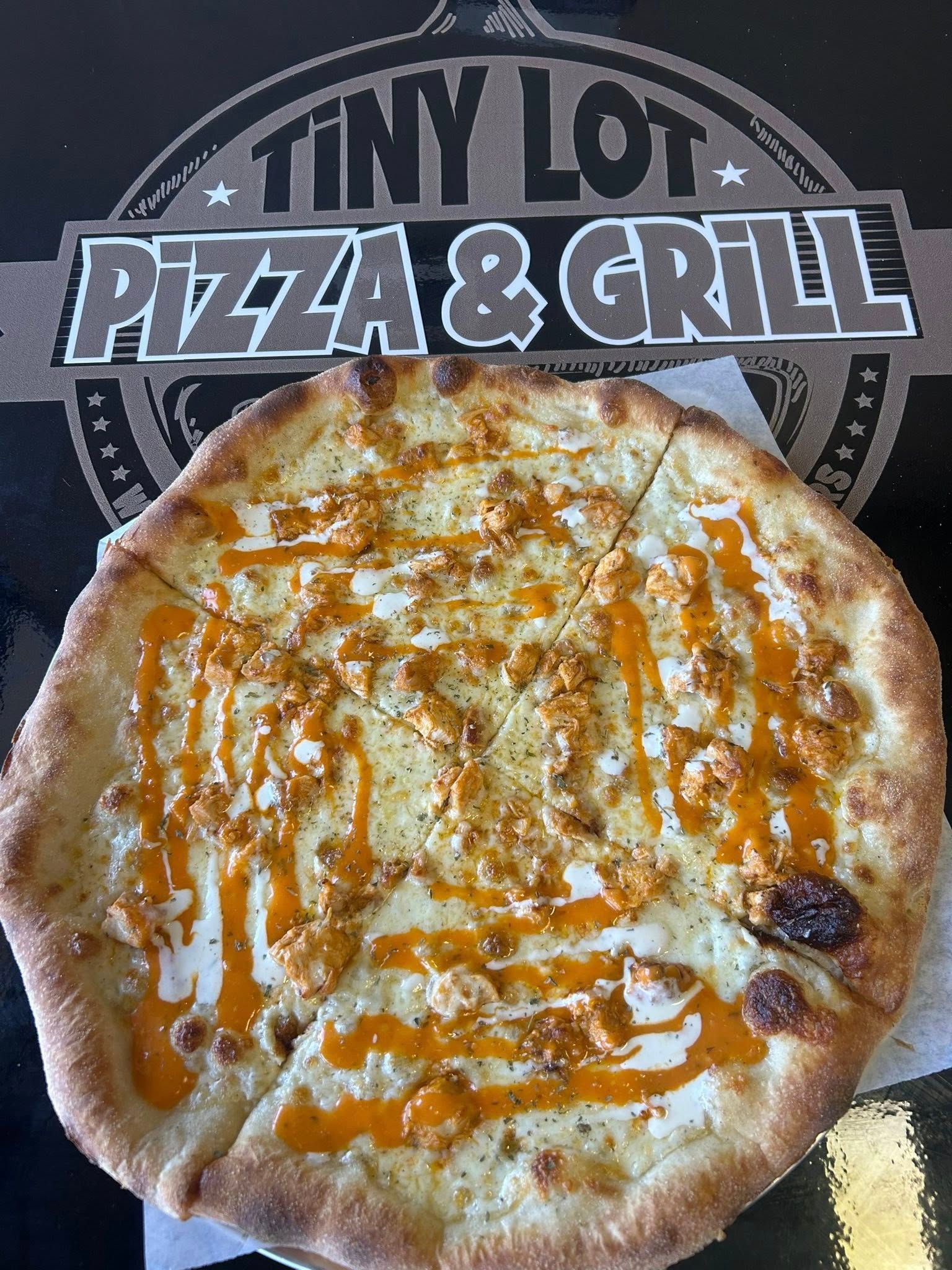 Cheese pizza on a Tiny Lot Pizza & Grill logo background