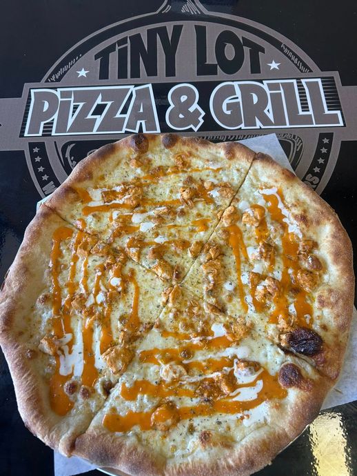 Cheese pizza in a box with Tiny Lot Pizza & Grill logo behind it