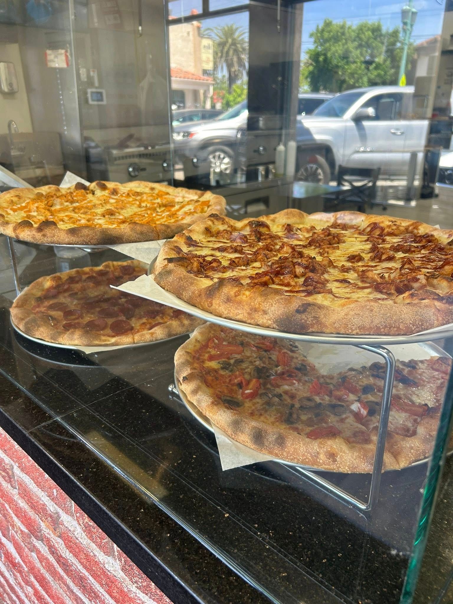 Several large pizzas displayed behind a glass case in a shop window.