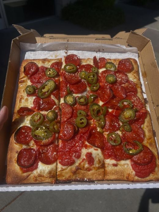 Deep-dish pizza in a cardboard box, topped with pepperoni and jalapeño slices.