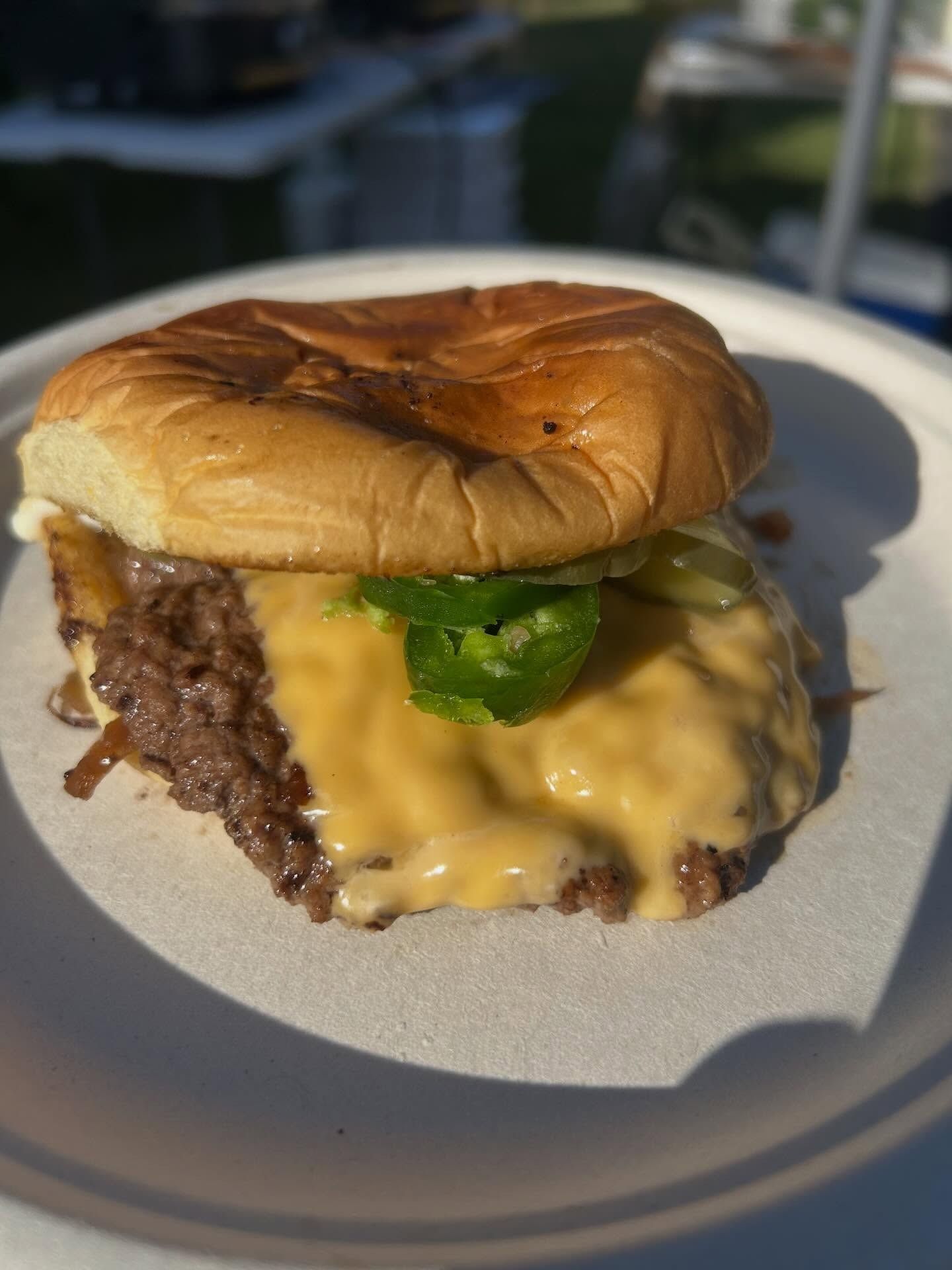 Close-up of a cheeseburger with melted cheese and a green pepper on a white plate outdoors