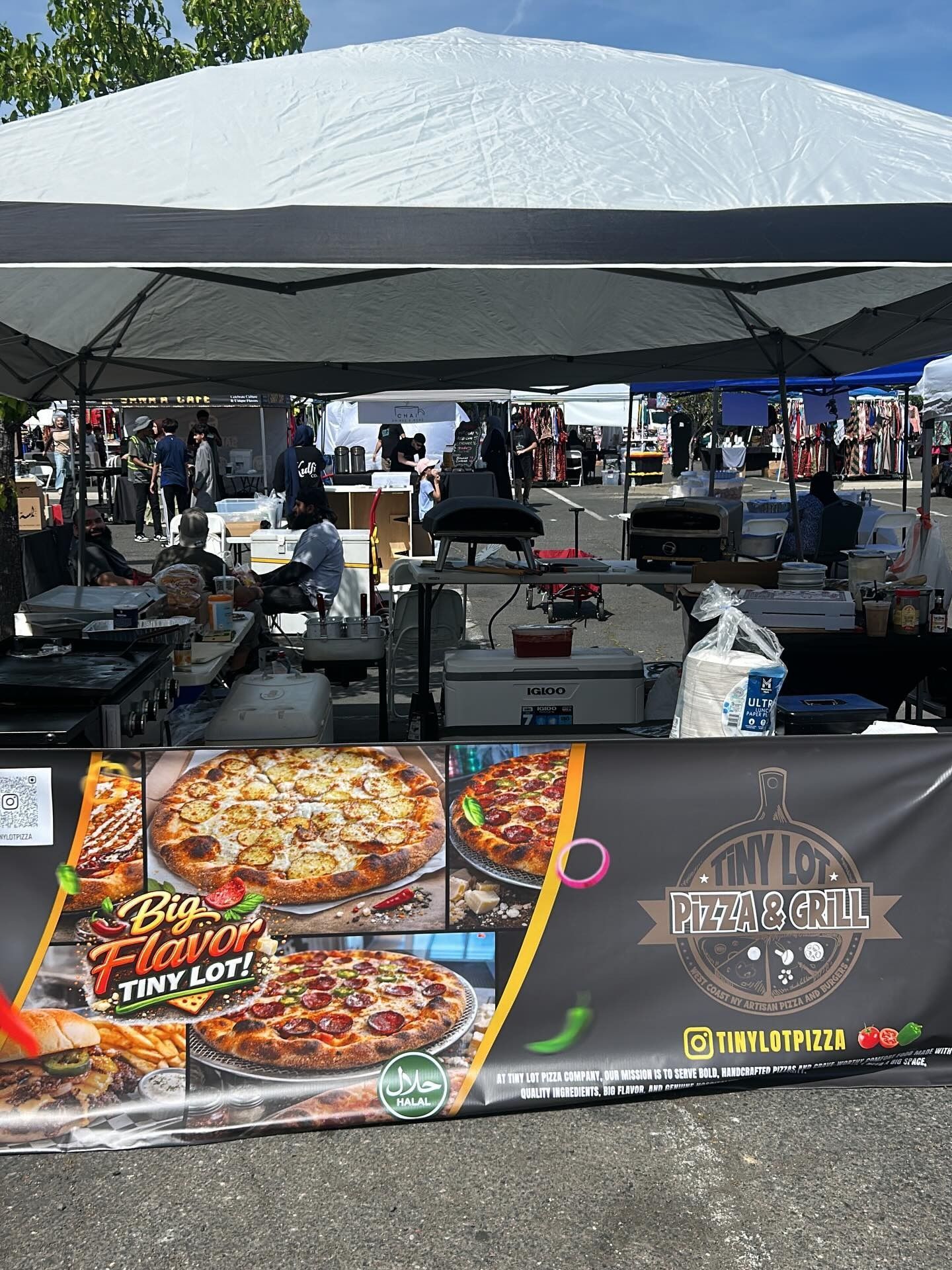 Outdoor fair booth with pizza banners, tables, and equipment under a canopy