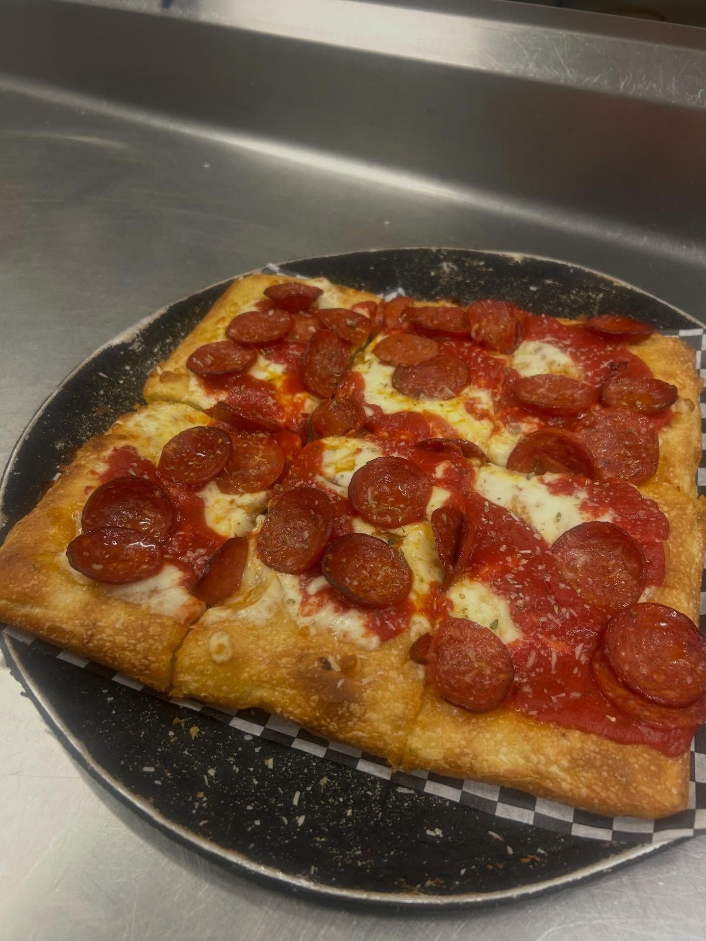 Pepperoni pizza slice on a black plate on a stainless-steel counter
