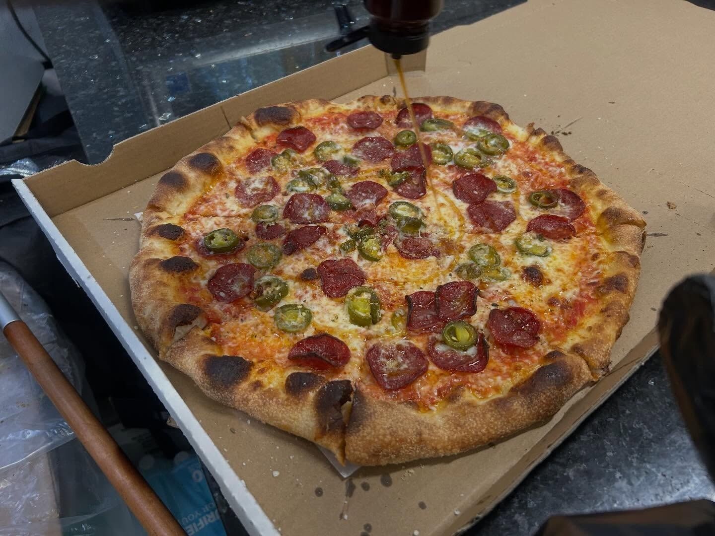 Pepperoni pizza on a cardboard box, with a metal spatula hovering above it in a kitchen setting