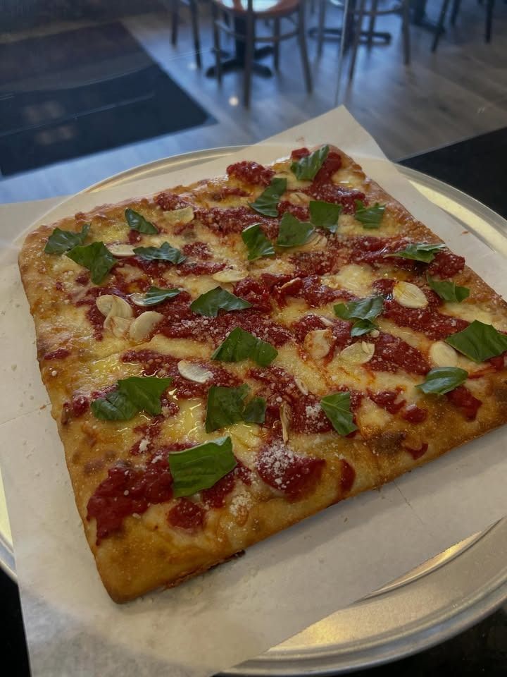 Square pizza topped with basil and pepperoni on a white plate in a café setting