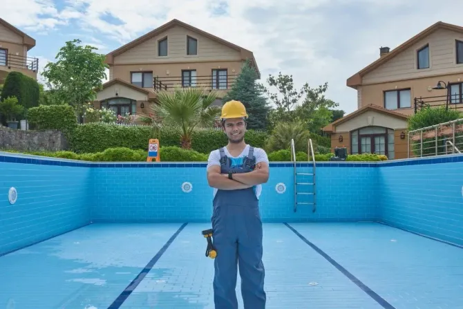 Maintenance worker in a hard hat standing in front of an empty tiled pool.