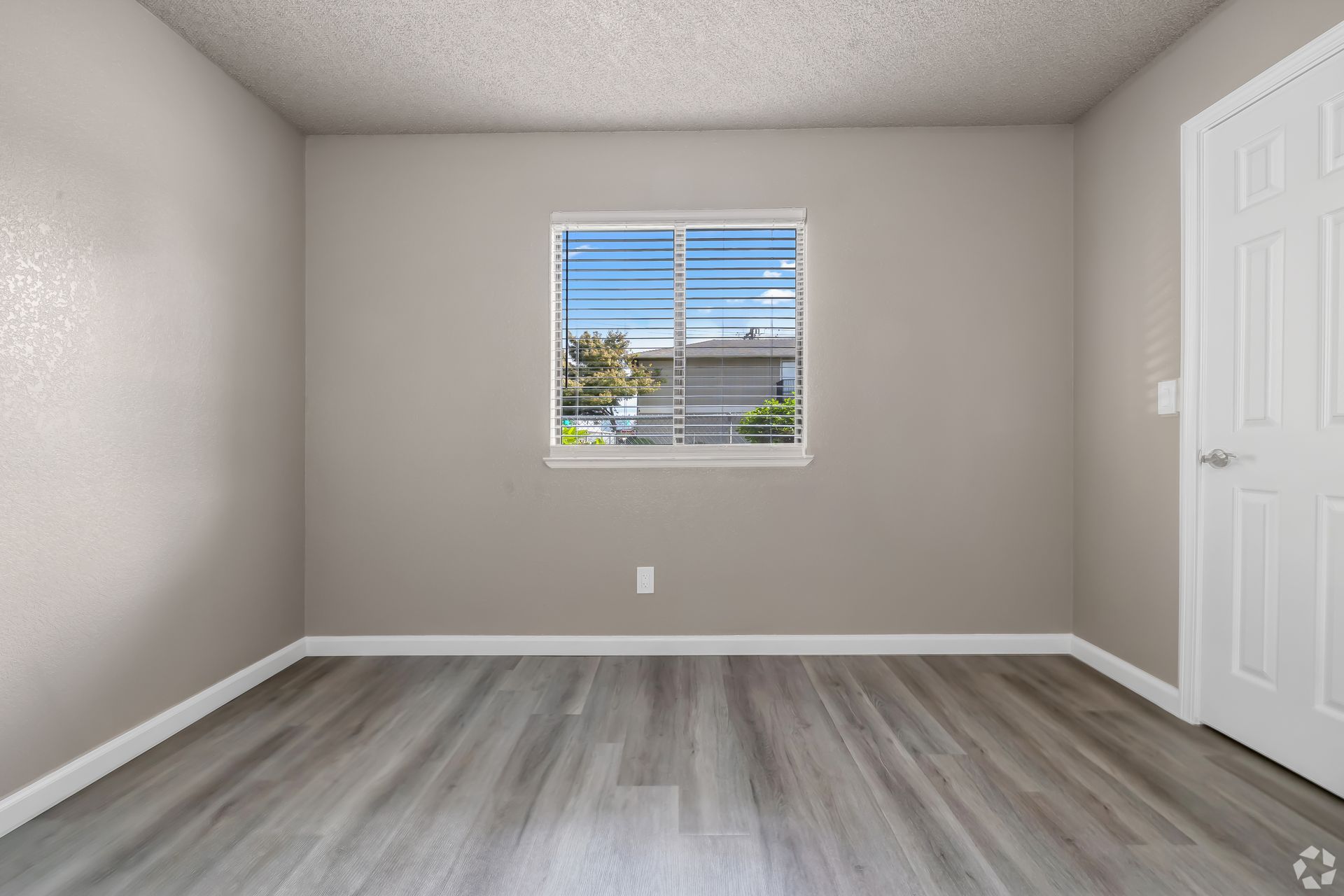 Empty room with gray walls, wood-look floor, window, white door.