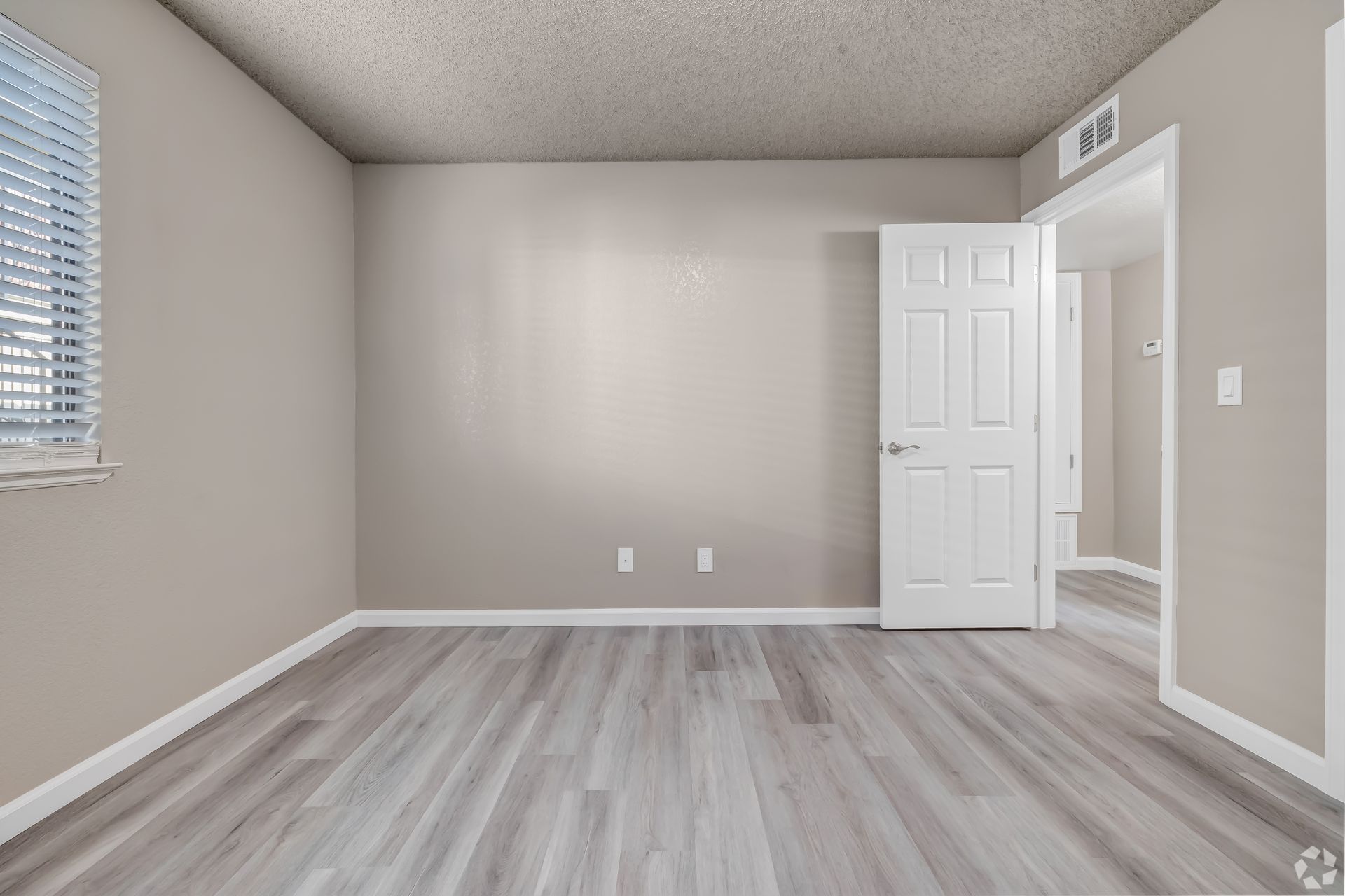 Empty bedroom with neutral walls, grey flooring, a window, and an open door.