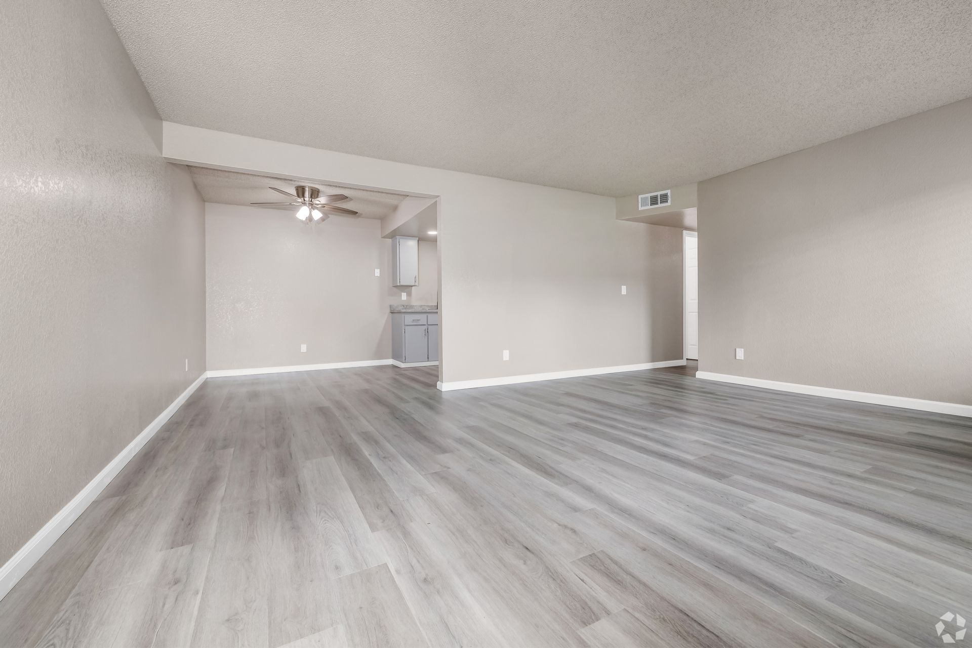 Empty living room with light gray wood-look flooring and neutral walls, doorway to a bathroom visible.