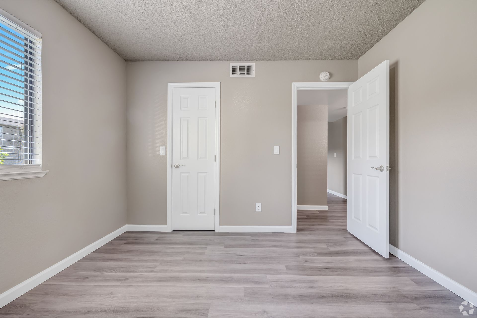 Empty room with light gray walls, wood-look floor, white doors and trim, a window, and an open doorway.