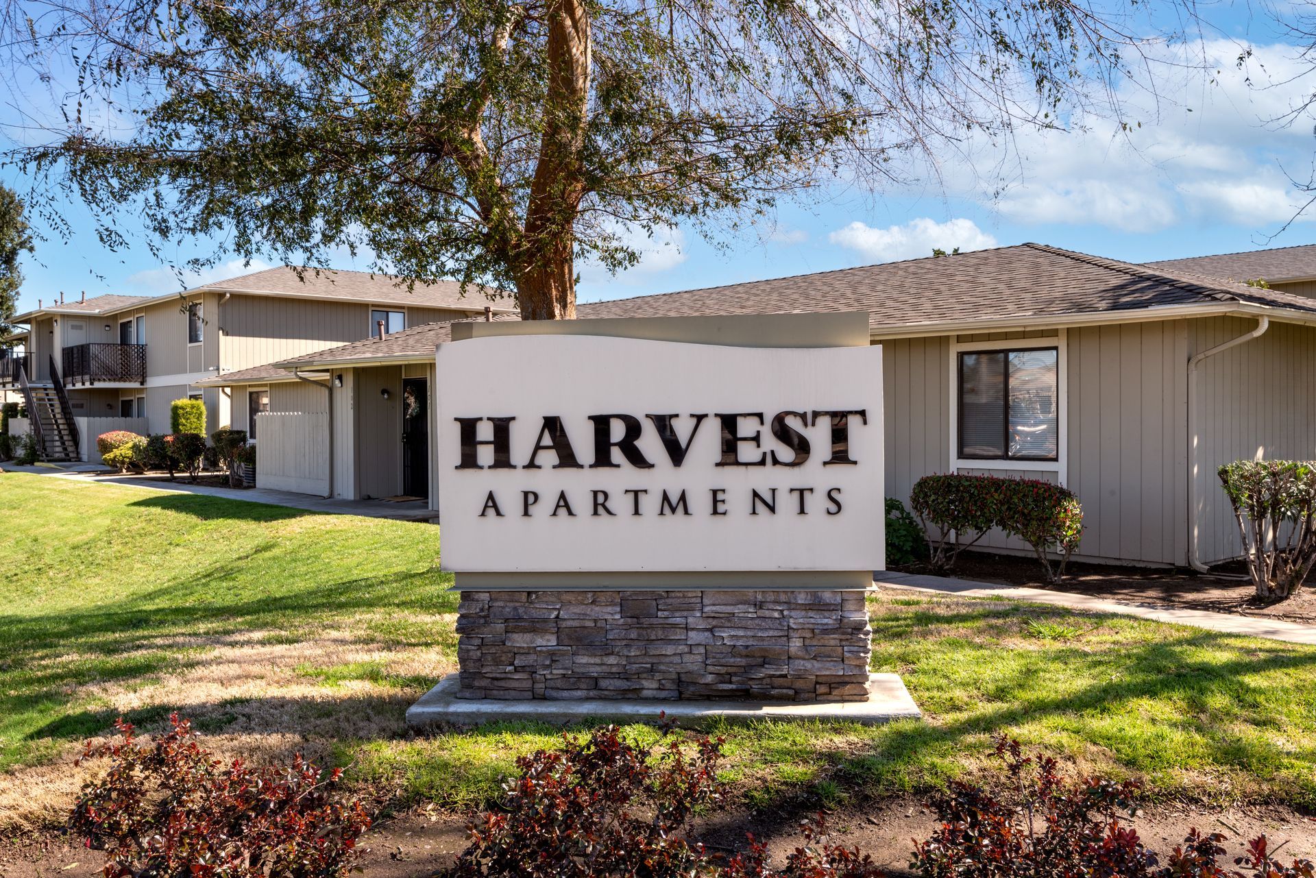 Sign for Harvest Apartments, beige buildings and green grass.