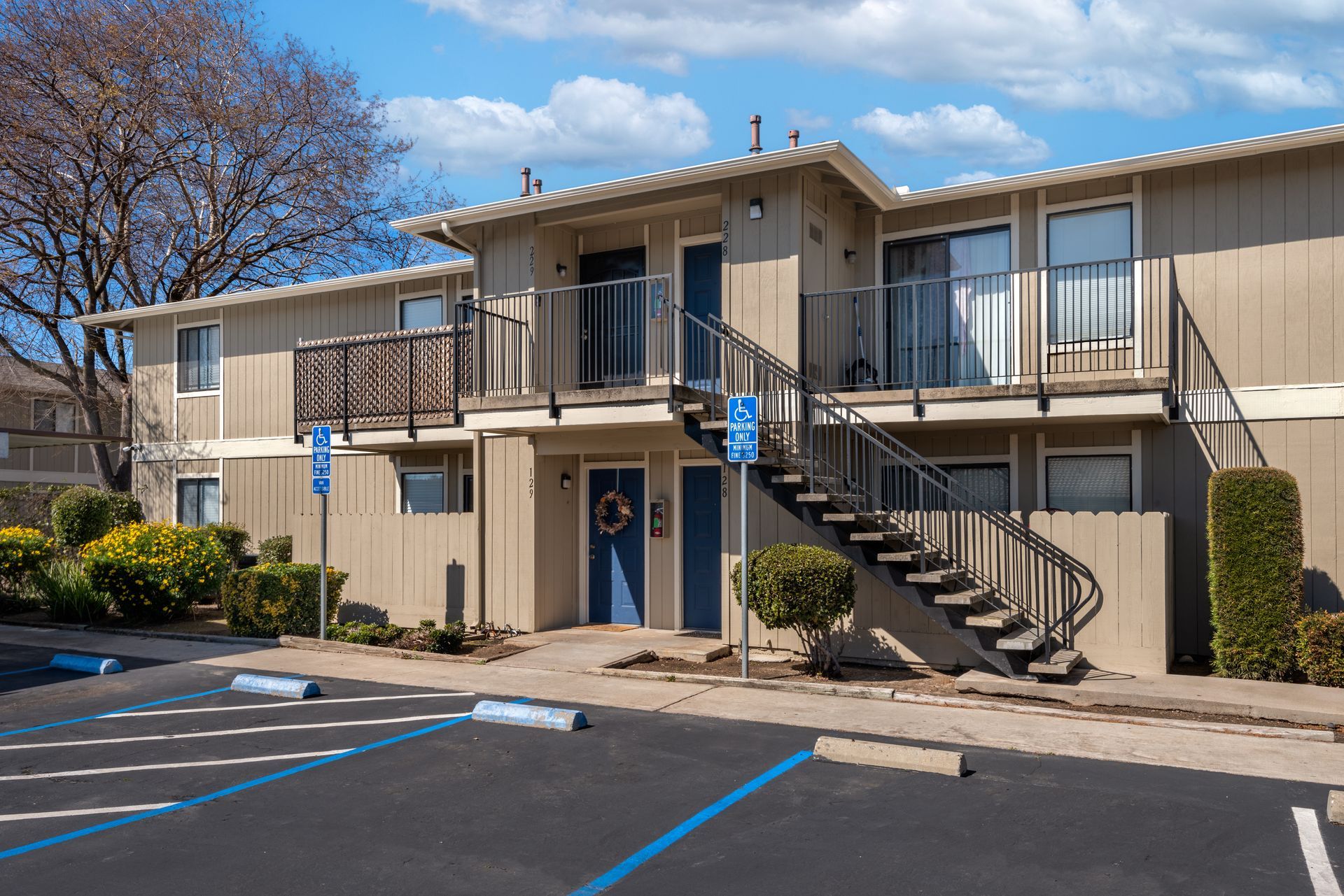 Apartment building with blue doors, exterior staircases, and reserved parking. Sunny day.