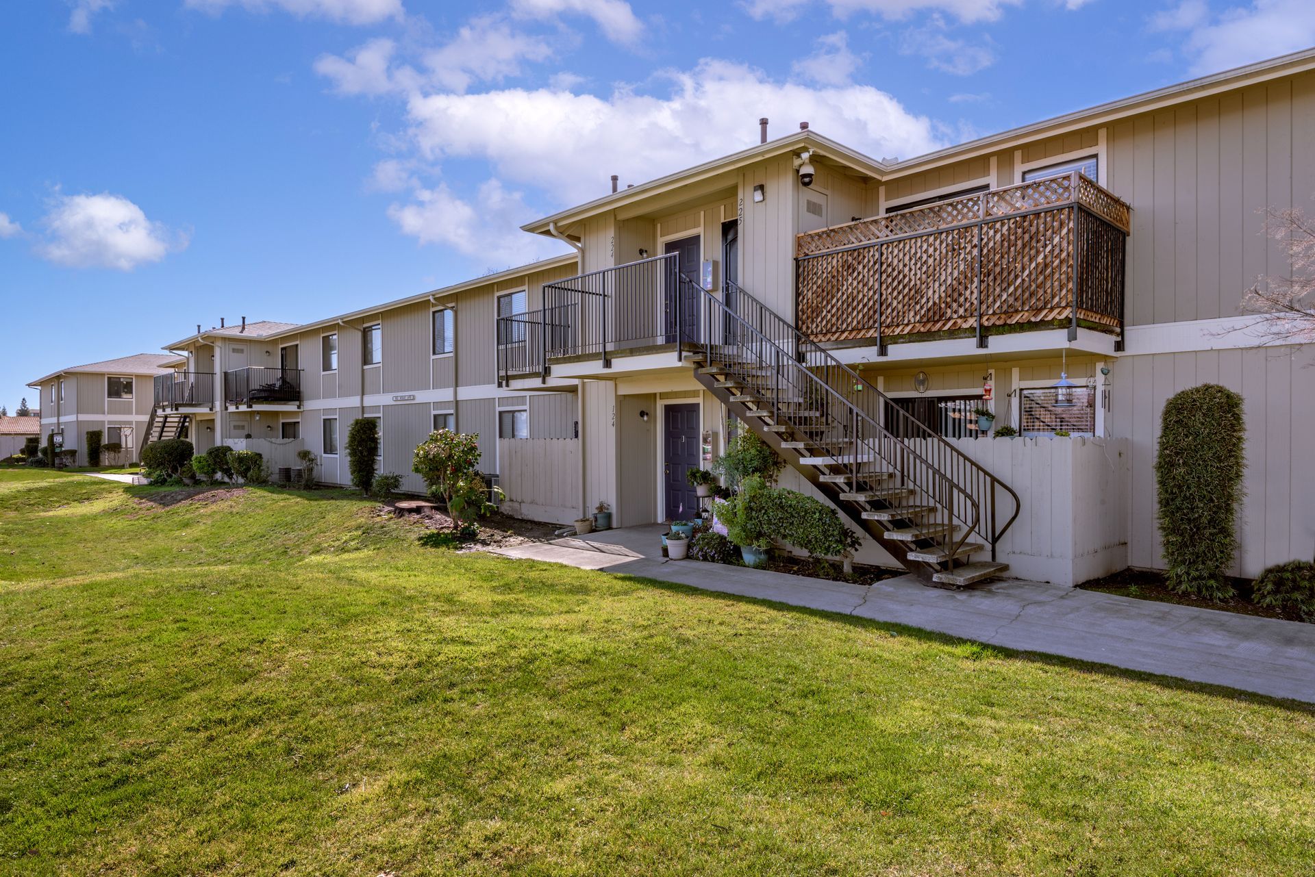 Apartment building with exterior stairs, green lawn, and blue sky.