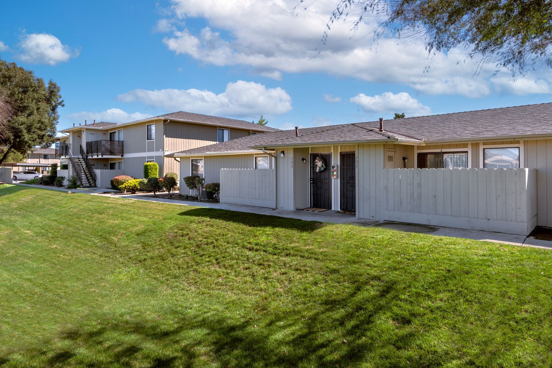 A row of townhouses with gray exteriors and grassy lawn under a blue sky.
