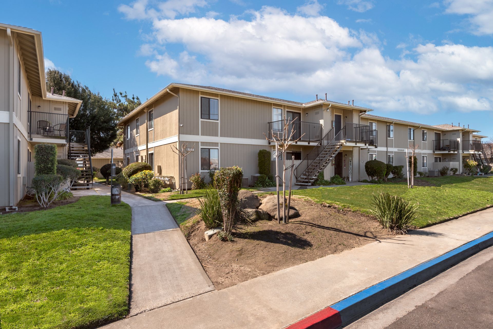 Apartment buildings with tan siding and green lawns on a sunny day.