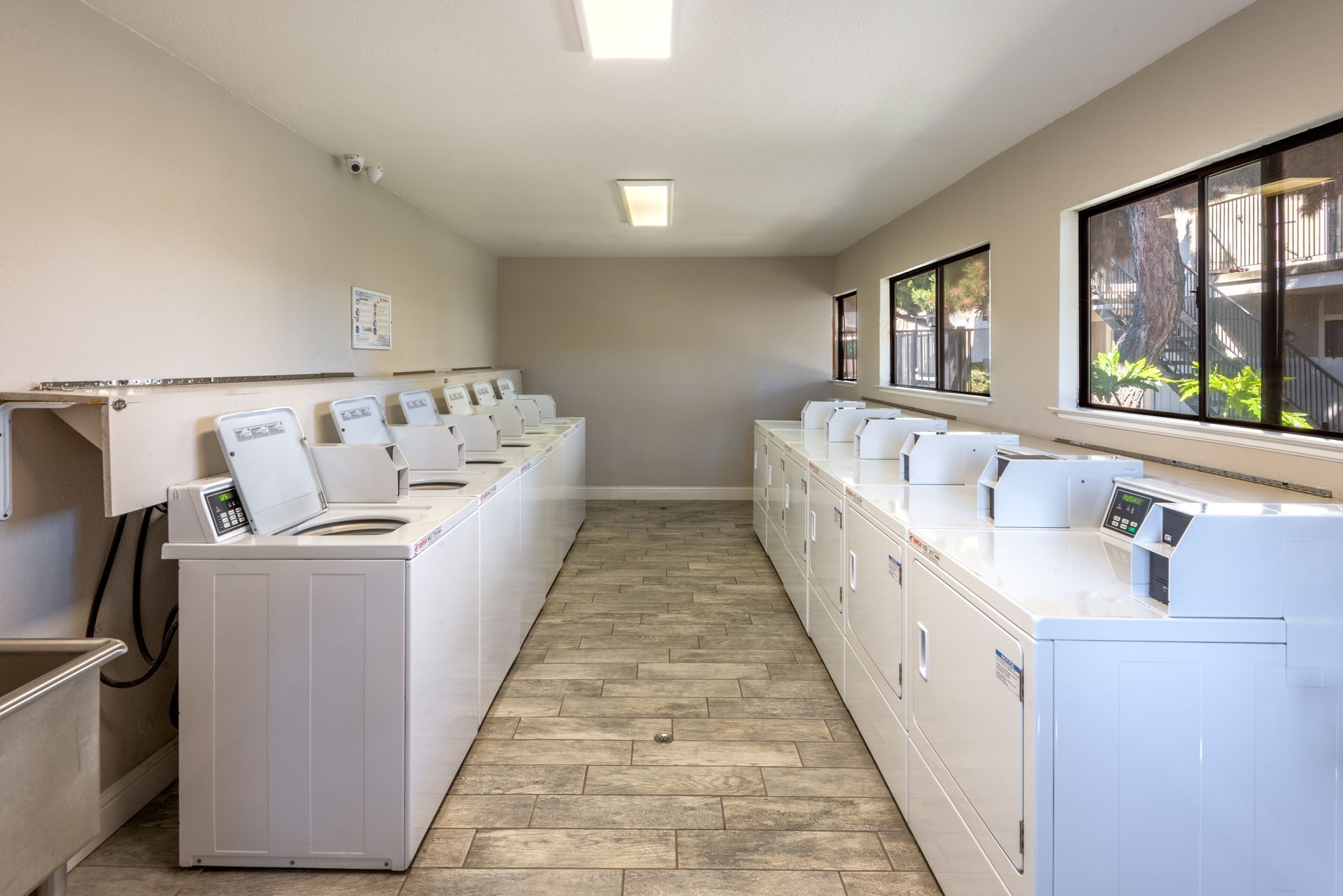 Rows of white washing machines and dryers in a laundry room. Windows provide natural light.