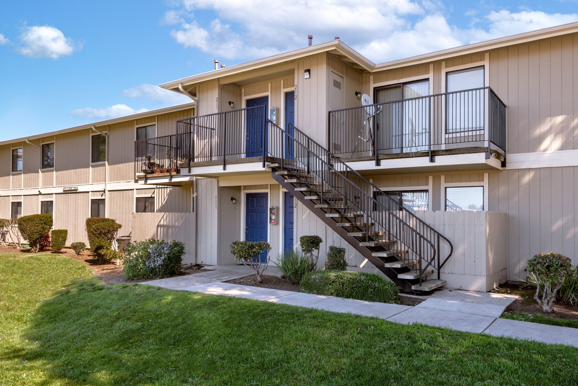 Two-story apartment building with blue doors, exterior stairs, and green lawn.
