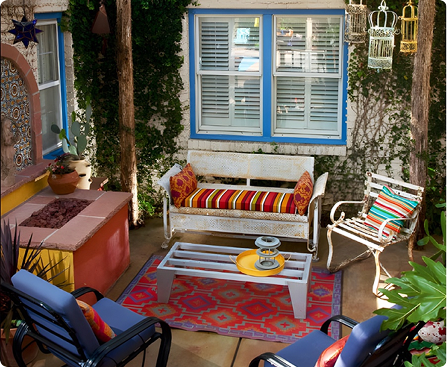 Cozy outdoor patio with seating, fireplace, rug, and vine-covered walls. Blue, white, and orange accents.