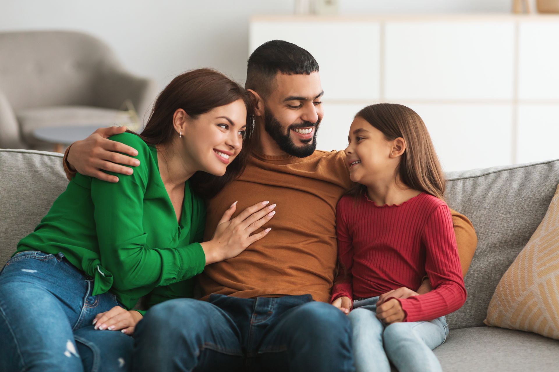 Three people sitting on a couch, smiling and embracing in a cozy living room.
