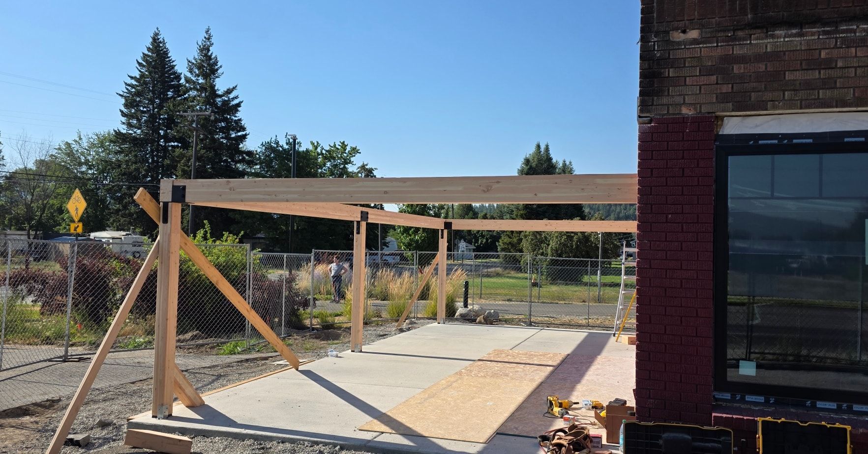 Wooden deck frame under construction beside a brick building on a sunny day