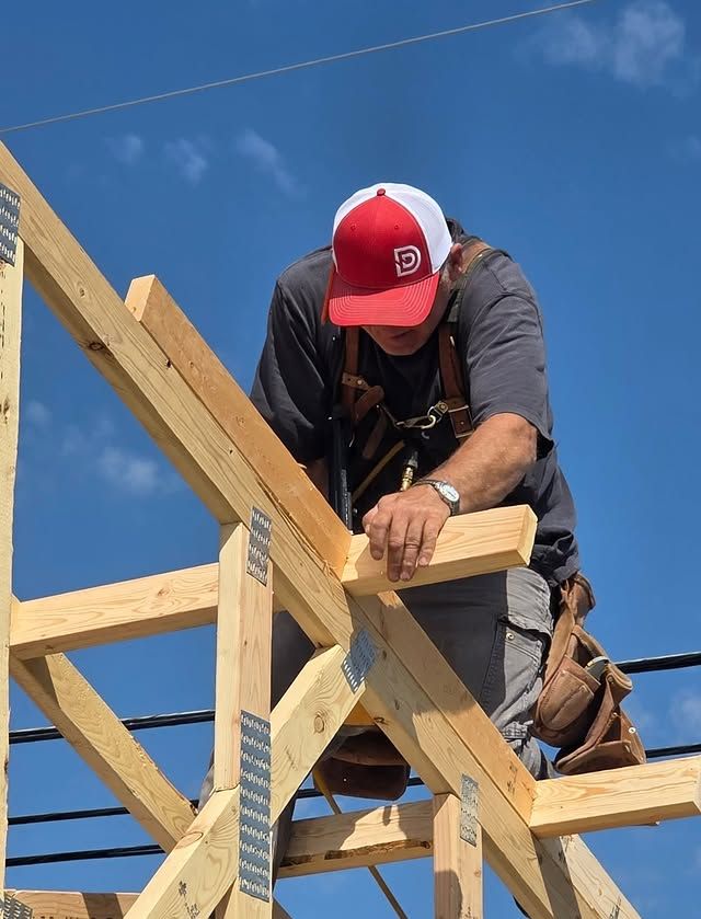 Worker in red cap securing wooden roof beams against a blue sky