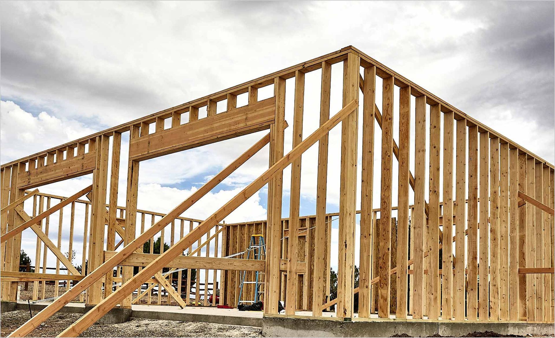 Unfinished room under construction with exposed wooden framing, windows, and a concrete floor