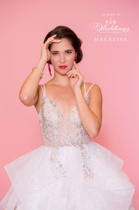 A woman in a white wedding dress is standing in front of a pink background.