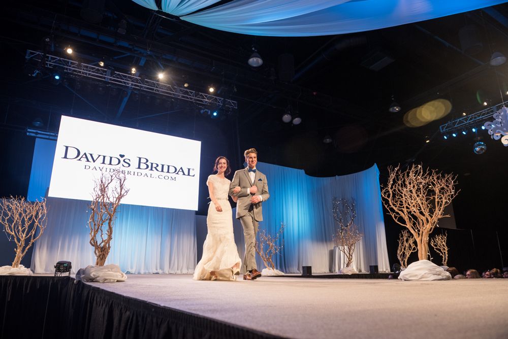 A bride and groom are walking down a runway at a wedding show.