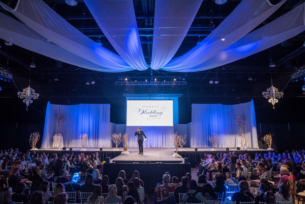 A man is standing on a stage in front of a crowd at a fashion show.